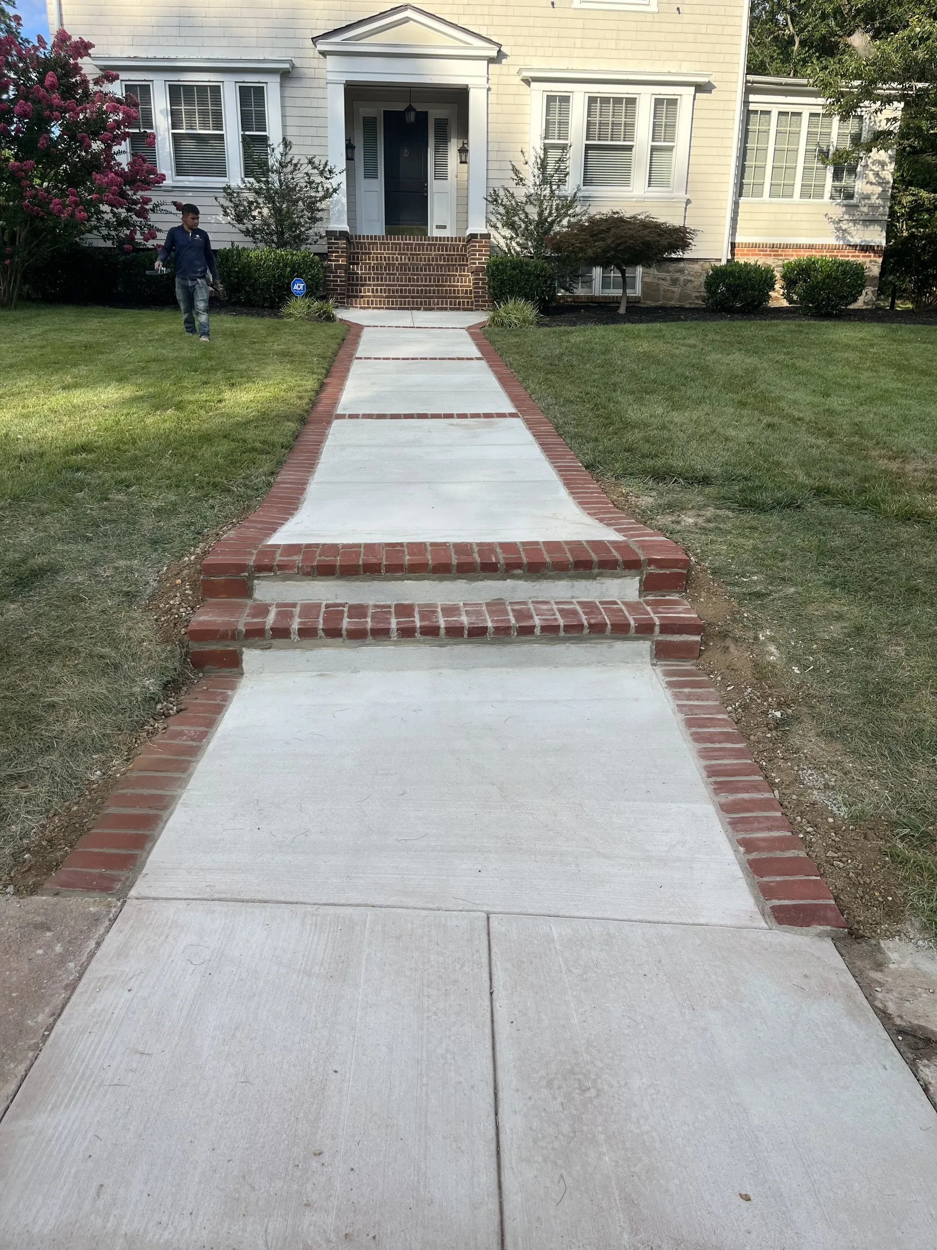 Concrete walkway with red brick borders and steps leading to the front entrance of a light yellow house