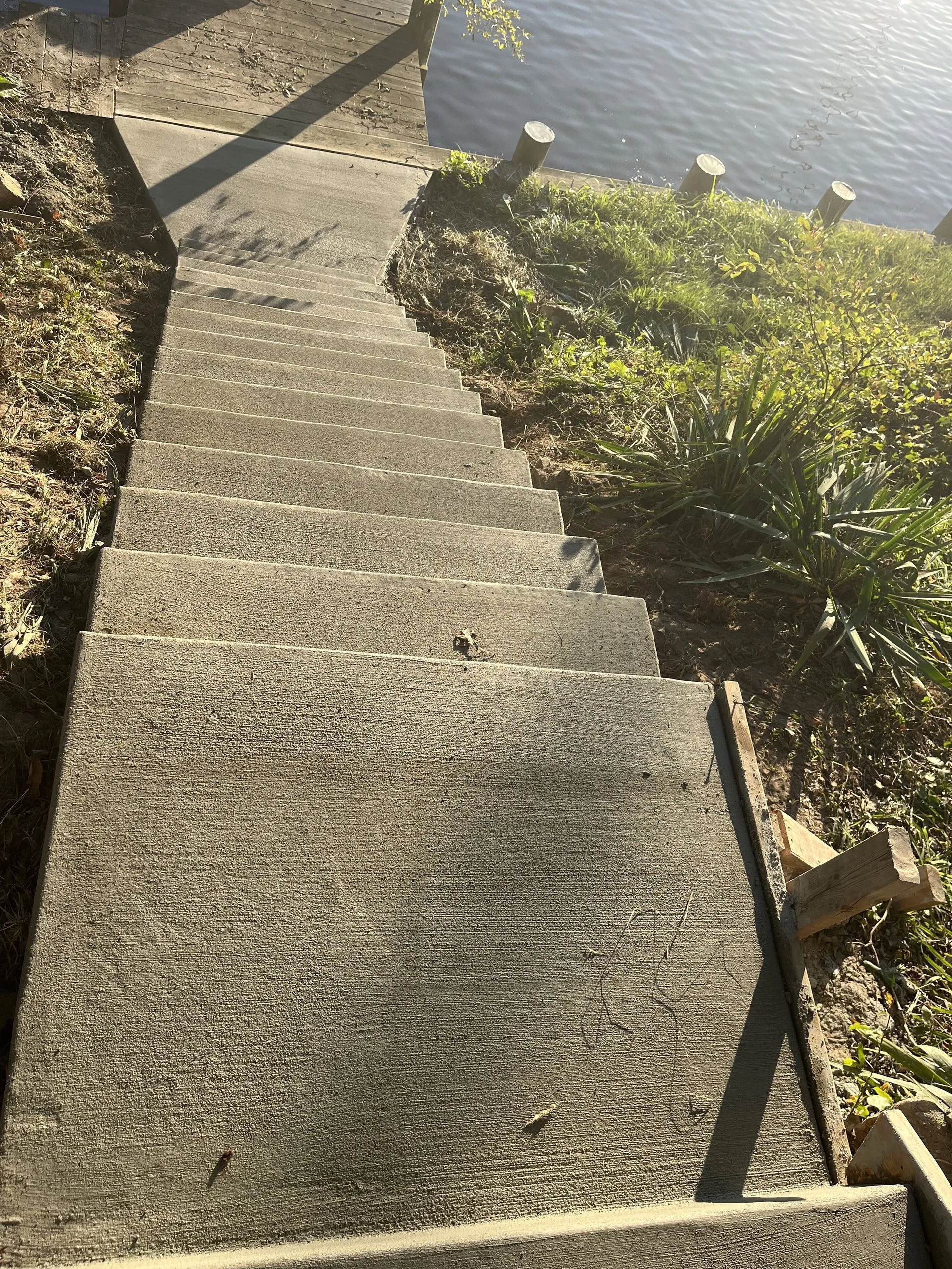 Freshly poured concrete staircase with broom-finished treads descending a grassy slope toward a wooden dock