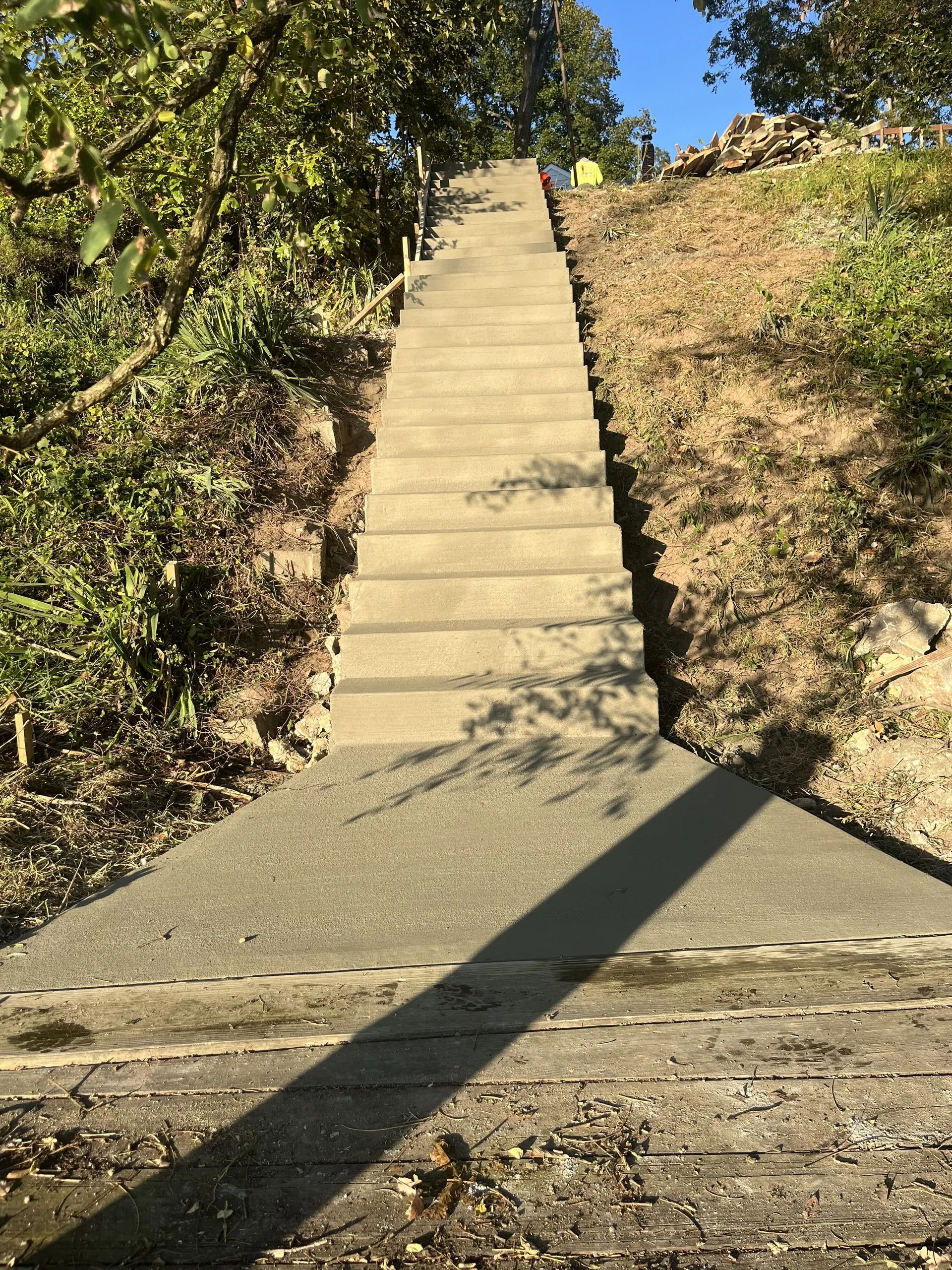 Newly poured concrete staircase ascending a grassy hillside with workers visible at the top