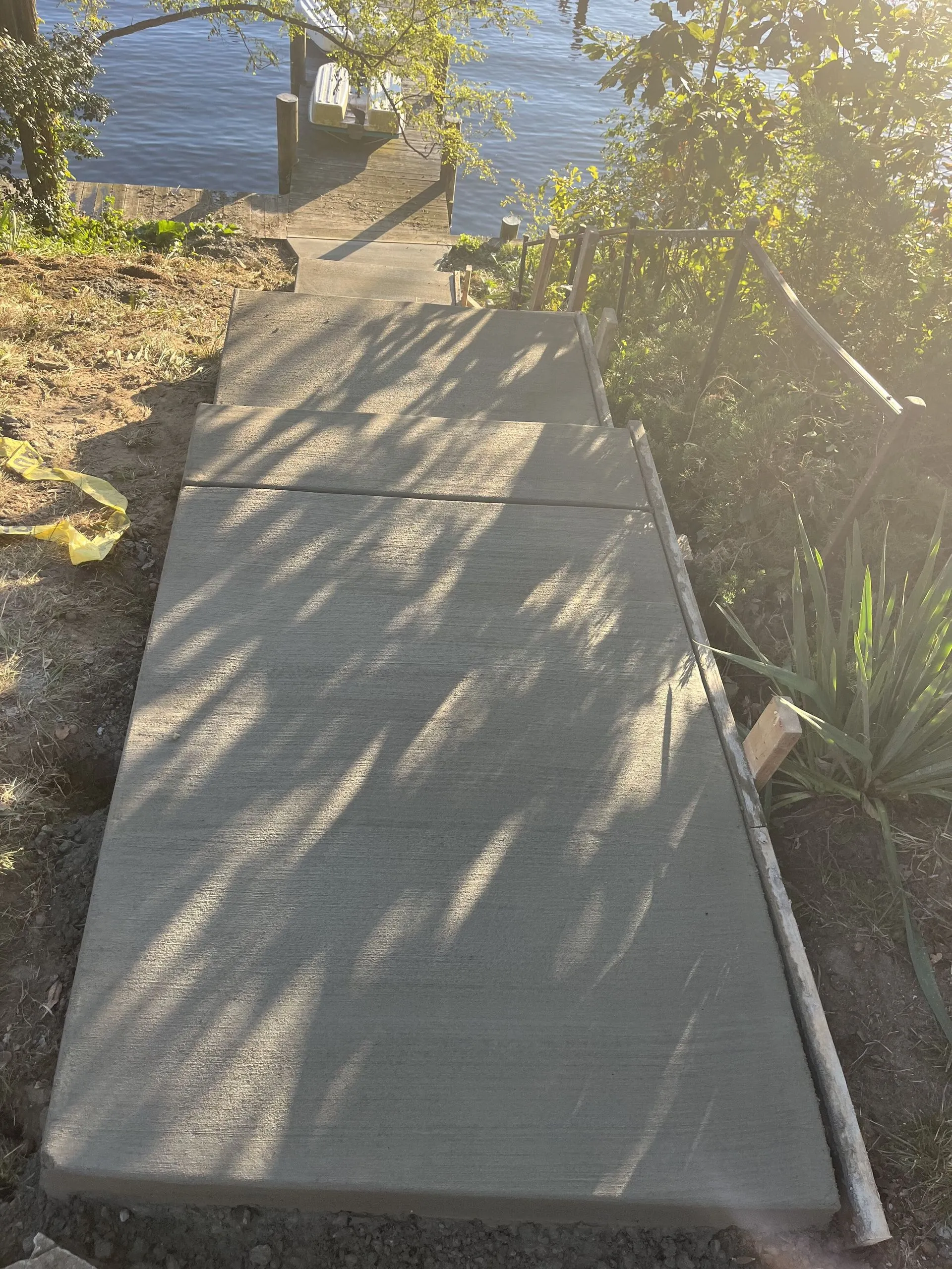 Newly poured concrete walkway leading down to a wooden dock on a lake in warm evening light