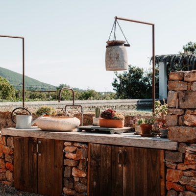 A rural outdoor kitchen with a cooking pot and cabinets on a concrete patio.